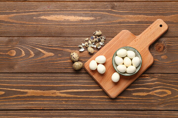 Board with bowl of boiled quail eggs and shells on wooden background