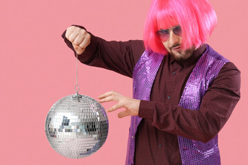 Handsome young man in wig with disco ball on pink background