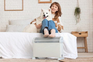 Young woman with cute Samoyed dog warming legs on radiator in bedroom