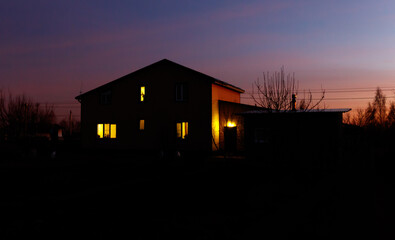 A house with a porch and a window is lit up at night