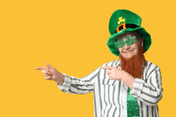 Senior woman in leprechaun hat and decorative glasses with red beard pointing at something on...