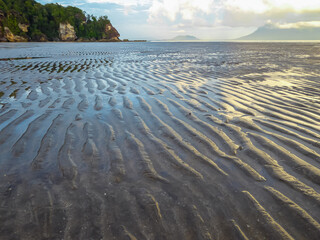 Wet sand beach sculpted with intricate ripple patterns by receding tide in Bako National Park,...