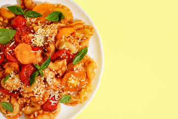 Plate of tasty pasta with tomato and basil on yellow background
