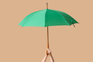 Female hand with umbrella on beige background