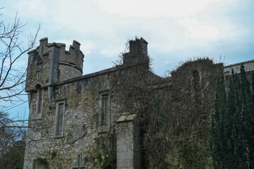 Grey stone castle stands under an overcast sky in Howth near Dublin, Ireland. Crenellated tower dominates the view. sense of history and age. Travel destination. Medieval landmark. Mystical atmosphere