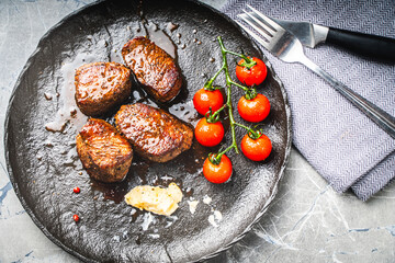 Filet mignon steaks with cherry tomatoes on a black mica plate, With gray napkin and cutlery. Top view