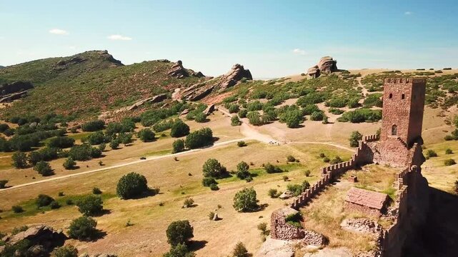 Aerial view of Castillo de Zafra, Spain, nestled amidst rugged terrain and lush greenery, showcasing its historic medieval architecture and natural surroundings under a vibrant blue sky