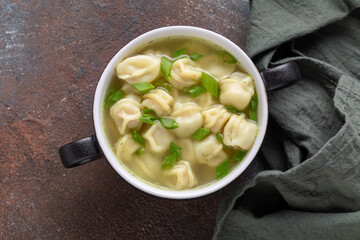 Homemade boiled dumplings or pelmeni with broth and scallion in a ceramic bowl on the table. Top view