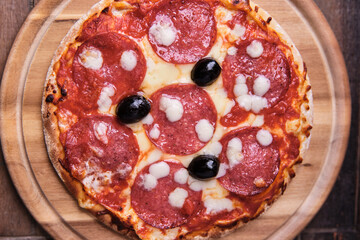 Pizza with salami and mozzarella cheese. Wooden background. Soft focus. Top view.