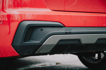 Close up of a red vehicle's rear bumper with parking sensors and diffuser
