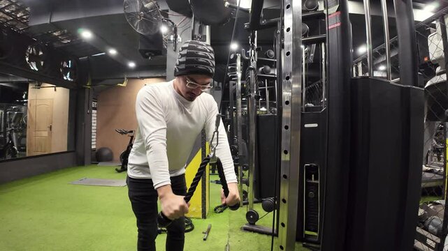 Young Man Doing Triceps Pushdowns with a Rope in an Empty Gym, with a Large Mirror and Gym Equipment in the Background, in Slow Motion