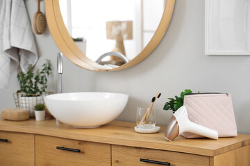 Modern photoepilator with cosmetic bag and houseplants on table near sink in bathroom