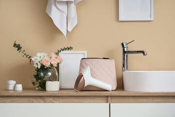 Modern photoepilator with cosmetic bag and flowers on table near sink in bathroom