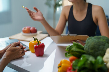 Nutritionist explaining healthy diet plan to patient during consultation in clinic, focus on fresh vegetables and fruits on table, promoting balanced nutrition and wellness