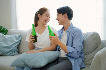 Asian young happy couple drinking beer sitting sofa in living room at home. sweet romantic relax time.