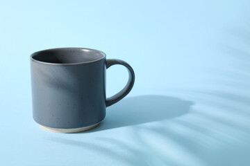 Stylish ceramic mug and palm leaf shadow on color background