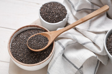 Bowls and spoon with chia seeds on white wooden background