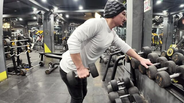 Young Man Performing Triceps Kickbacks with a Dumbbell in the Gym, One Hand on the Dumbbell Rack, with a Mirror in Front, Captured in Slow Motion