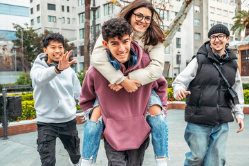 Four happy multiracial teens enjoying outdoor fun, with one boy giving a piggyback ride to a girl...