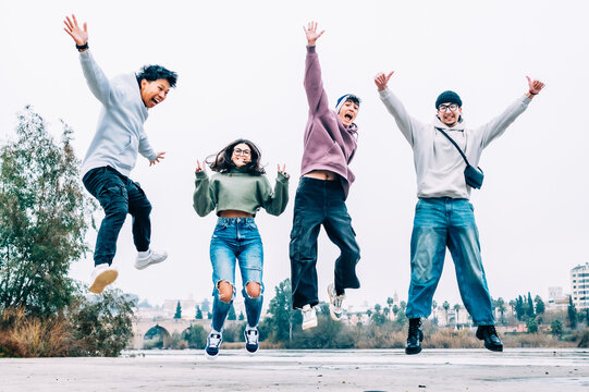 Four cheerful multiracial friends jumping together outdoors, radiating happiness and showcasing their strong bond while enjoying a carefree moment in the vibrant city 