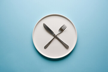 Top view of empty ceramic white plate and cutlery on blue background
