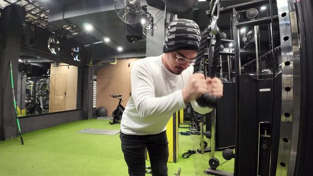Young Man Performing Triceps Pushdowns with a Rope in an Empty Gym, Featuring a Large Mirror and Gym Equipment in the Background, Captured in Slow Motion