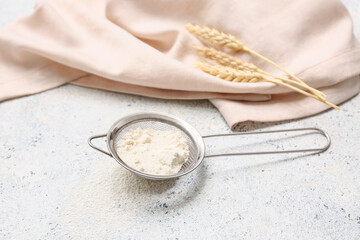 Metal sieve with flour, spikelets and napkin on light background