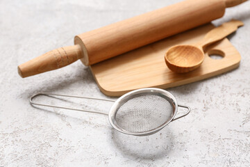 Metal sieve, wooden board, rolling pin and spoon on grunge background