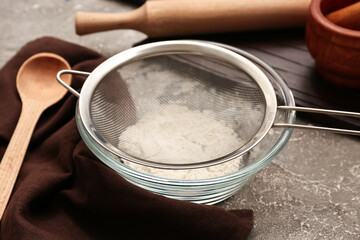 Metal sieve in bowl with flour and kitchen utensils on grunge background, closeup