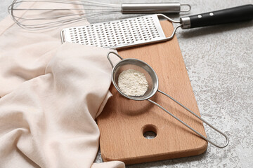 Metal sieve with flour, wooden board, grater, whisk and napkin on grunge background