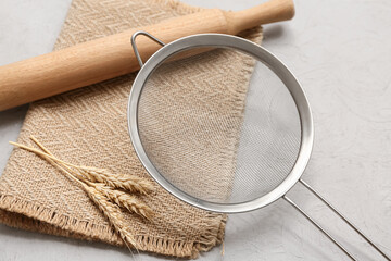 Metal sieve, rolling pin, napkin and spikelets on grunge background, closeup
