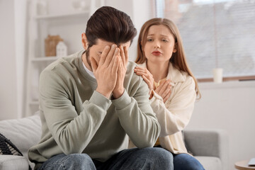 Young woman apologizing to her upset husband on sofa at home
