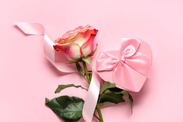 Composition with rose flower, silk ribbon and heart-shaped gift box on pink background. Valentine's Day celebration.
