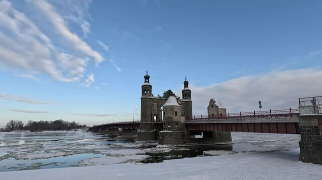 Stone bridge over the river with floating ice floes. Landscape of a winter sunny day.