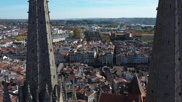 Drone flying around gothic spiers of Bayonne Cathedral with cityscape, France. Aerial lateral view