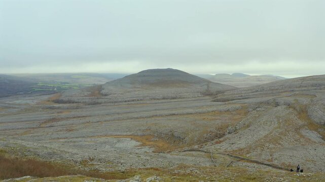 Aerial dolly shot of limestone hills in Burren National Park, featuring hikers admiring the scenery