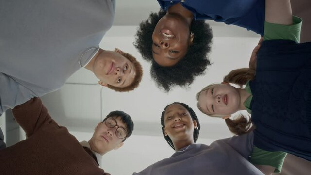 Bottom view shot of young African American woman and diverse zoomers hugging each other forming circle and looking at camera during teambuilding practice