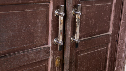 Obraz premium Close-up of a rustic wooden door with metal handles showing signs of wear and rust