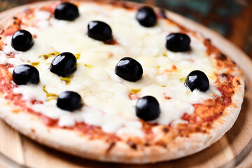 Pizza with mozzarella cheese and black olives on wooden background. Soft focus. Close up