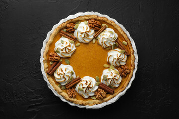 Delicious homemade pumpkin pie in baking dish on black textured table, top view