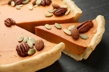 Pieces of tasty homemade pumpkin pie with seeds and nuts on black table, closeup