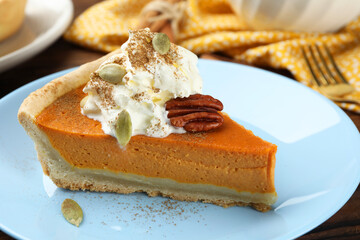 Piece of tasty homemade pumpkin pie with whipped cream, seeds and pecan nut on table, closeup