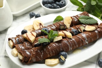 Delicious chocolate crepes with banana and blueberries served on white marble table, closeup