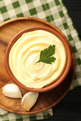 Delicious mayonnaise sauce in bowl and garlic on black table, top view