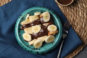 Delicious crepes with banana and chocolate paste on table, flat lay