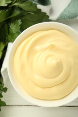 Delicious mayonnaise sauce in bowl and parsley on white wooden table, top view