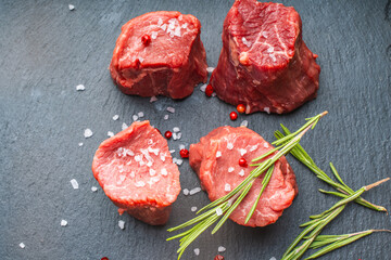 Raw filet mignon steaks with coarse salt and rosemary on a black mica board. Top view