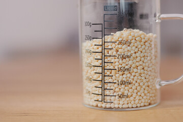 Raw quinoa grains pouring into glass storage jar in the kitchen, copy space. Healthy vegetarian...