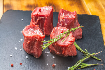 Raw filet mignon steaks with coarse salt and rosemary on a black mica board on a wooden background