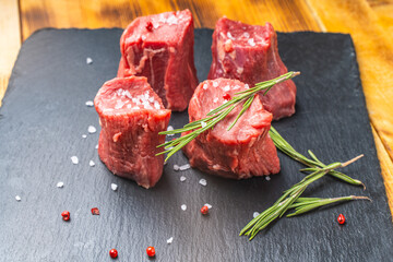 Raw filet mignon steaks with coarse salt and rosemary on a black mica board on a wooden background